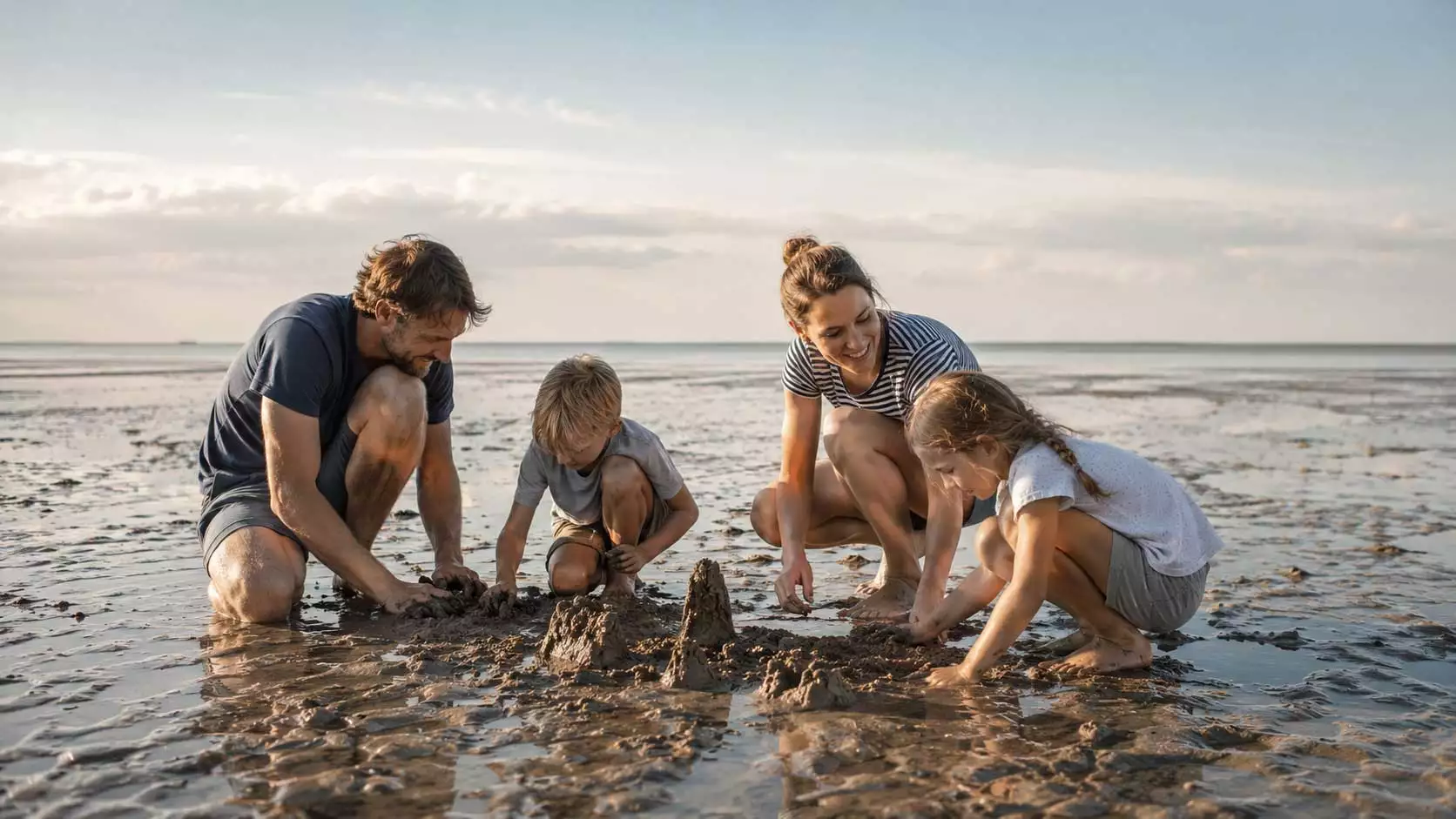 Familie baut gemeinsam Sandburgen im Watt auf Nordstrand